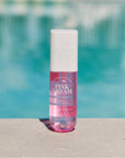 A bottle of Pink Dream body mist with pink liquid visible, placed on a surface with a pool in the background.