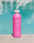 Pink bottle of Dupes & Co. body wash with a pool in the background