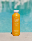 Orange bottle of Dupes & Co. body wash with a pool in the background