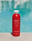 Red bottle of Dupes & Co. body wash with a pool in the background