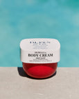 Jar of Dupes & Co. Body Cream with a red interior on a light blue background