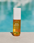 A bottle of Sun Bliss body mist with pistachio and vanilla scents, positioned near a poolside.
