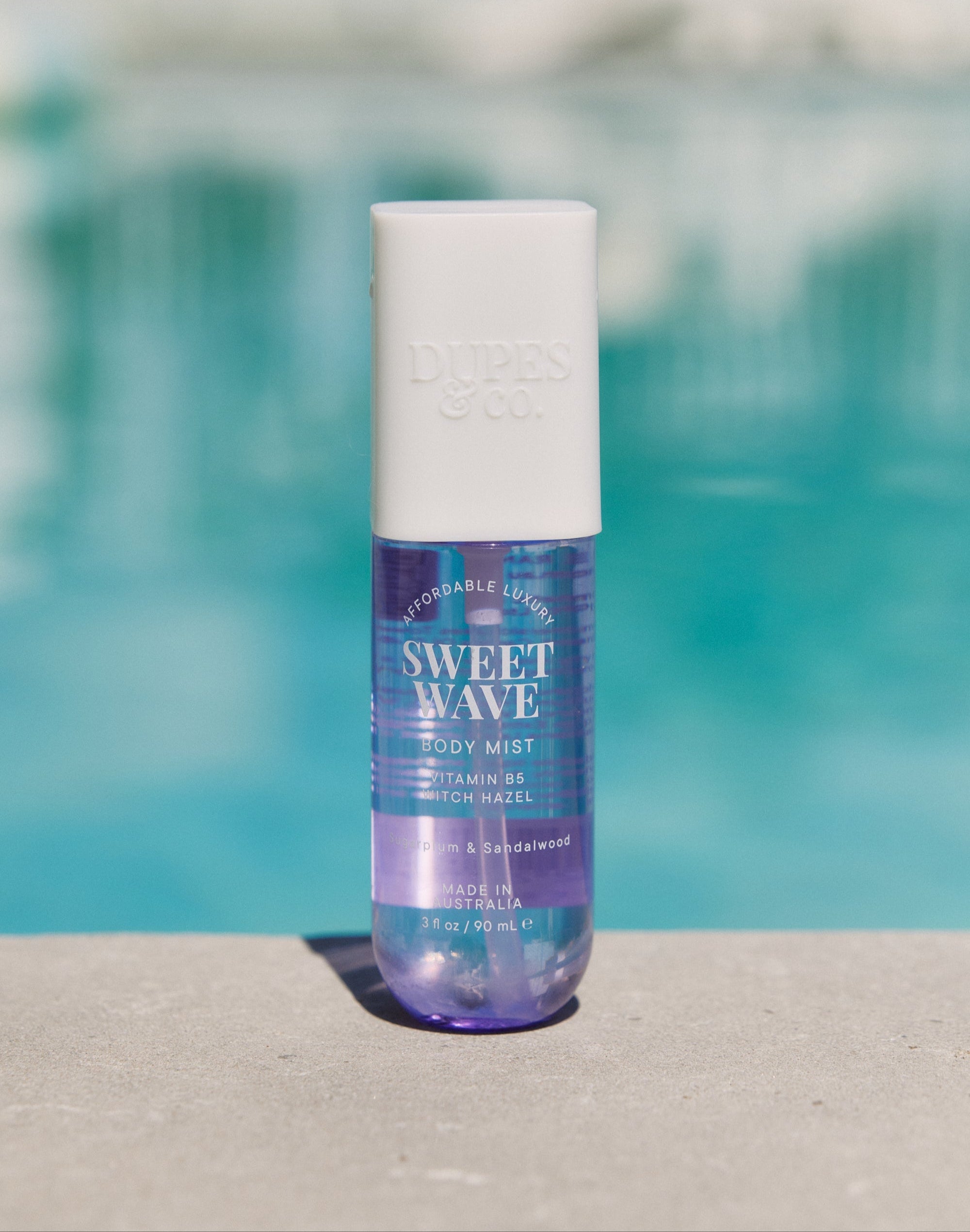A bottle of Sweet Wave body mist with plum and vanilla orchid, placed near a poolside.