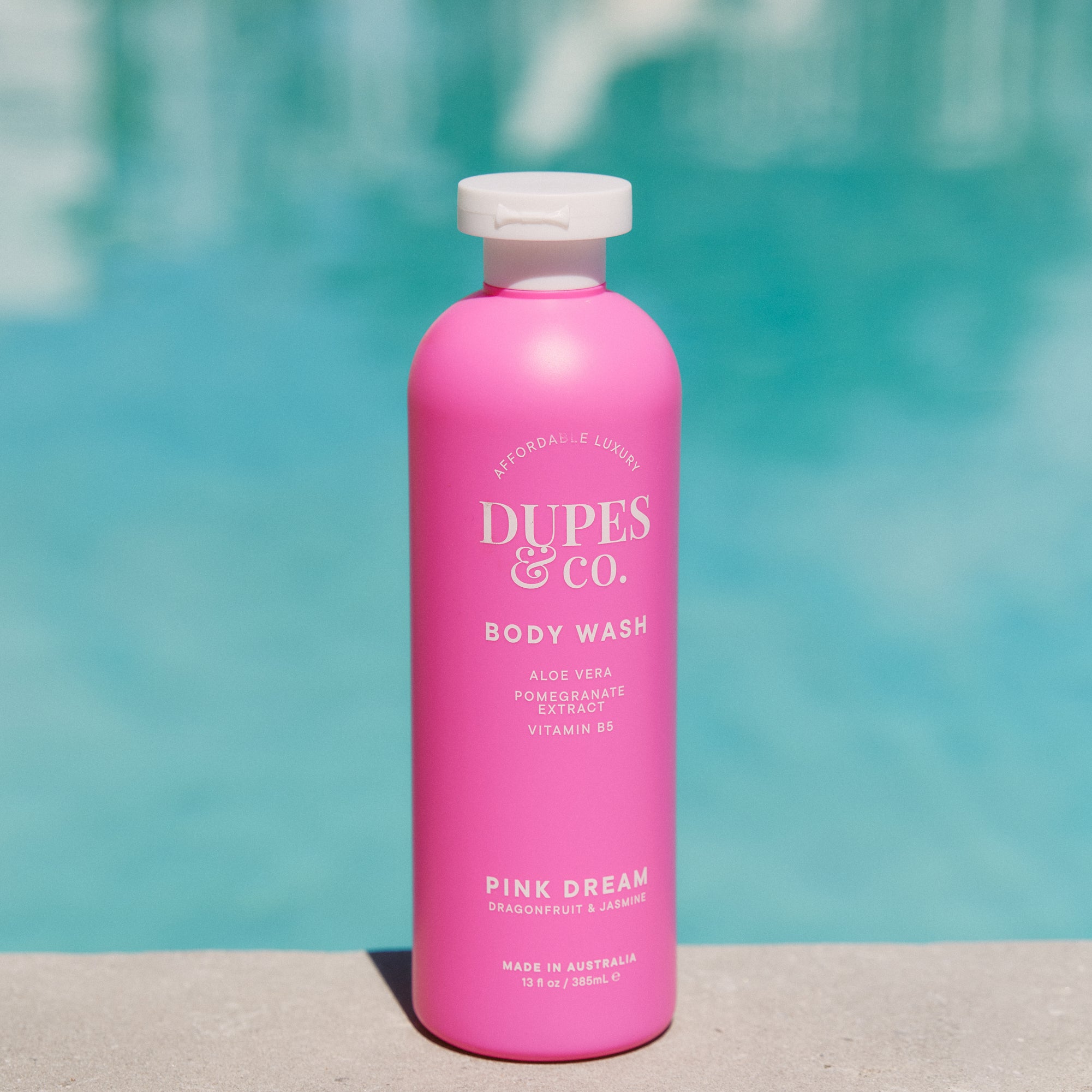 Pink bottle of Dupes & Co. body wash with a pool in the background