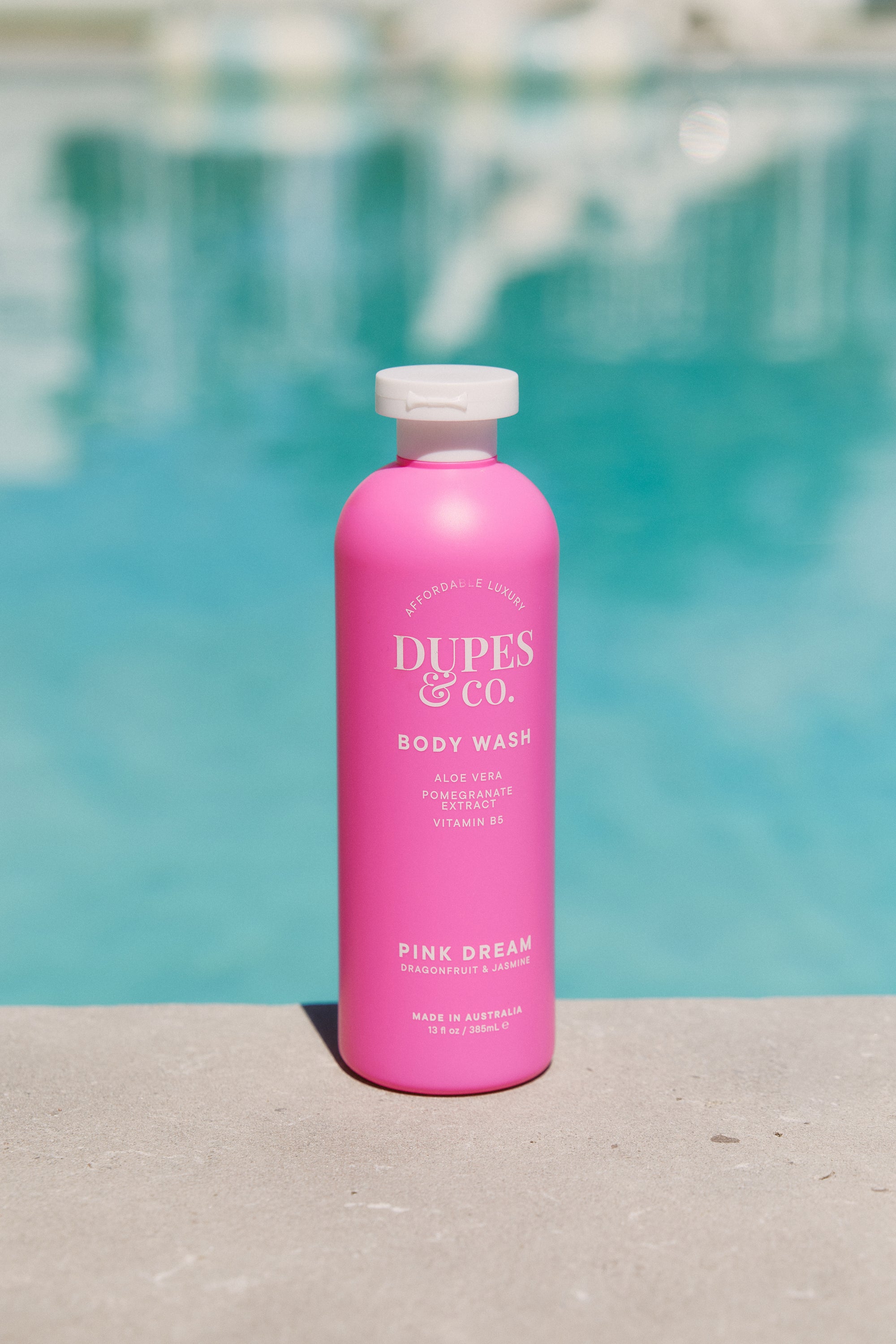 Pink bottle of Dupes & Co. body wash with a pool in the background
