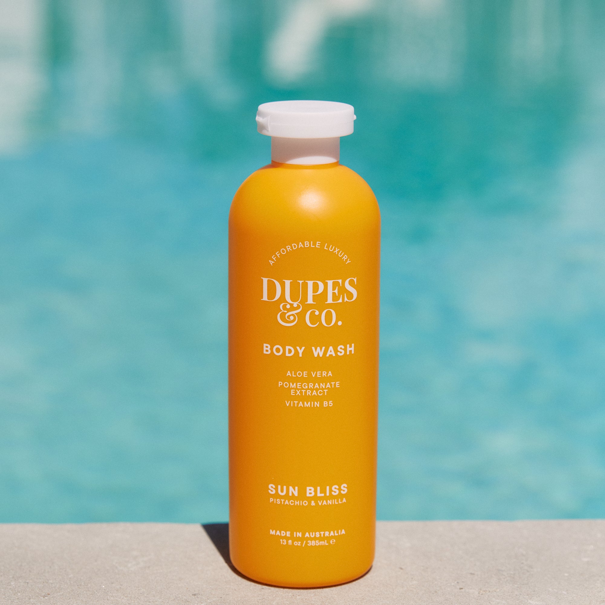 Orange bottle of Dupes & Co. body wash with a pool in the background