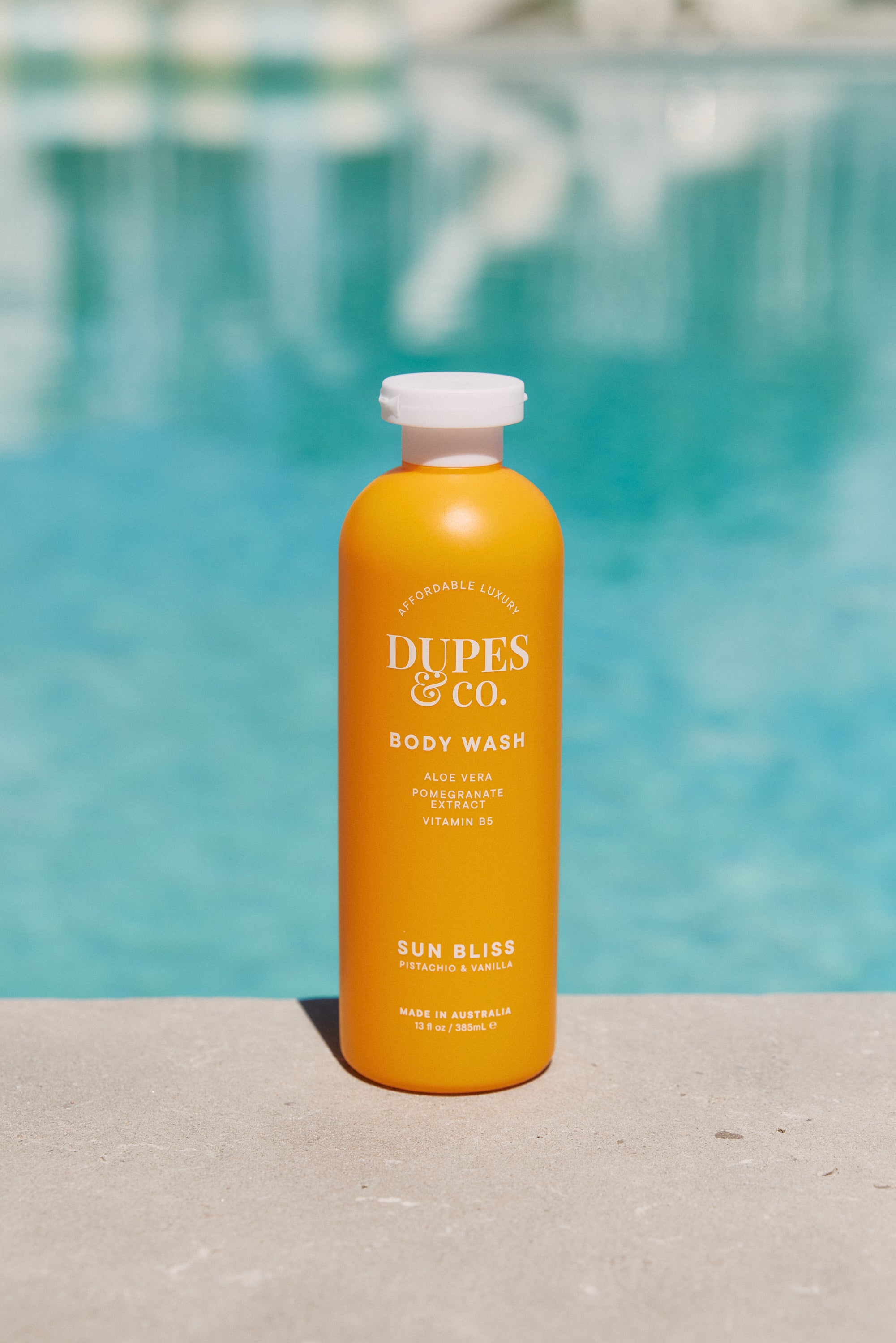 Orange bottle of Dupes & Co. body wash with a pool in the background