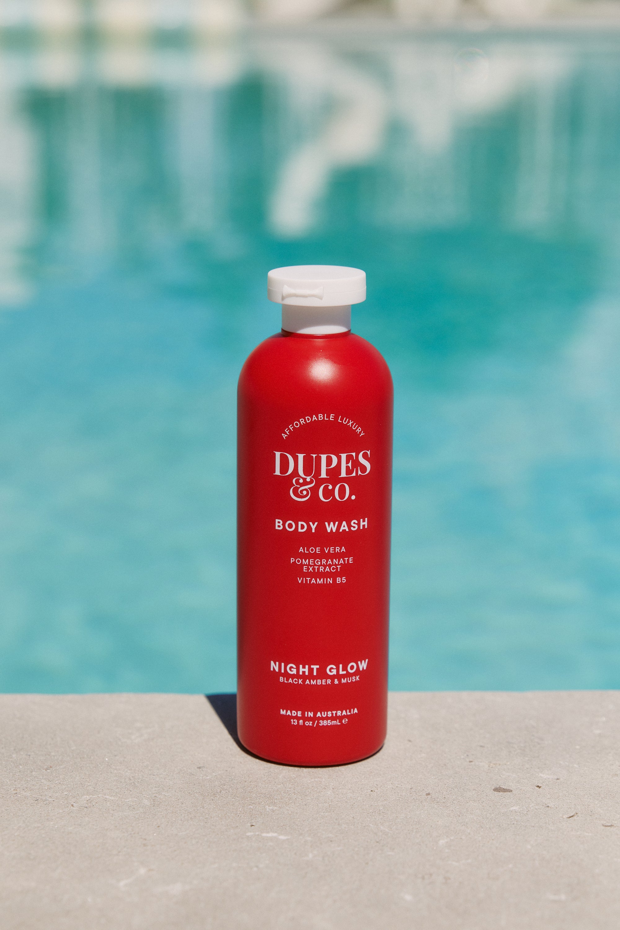 Red bottle of Dupes & Co. body wash with a pool in the background