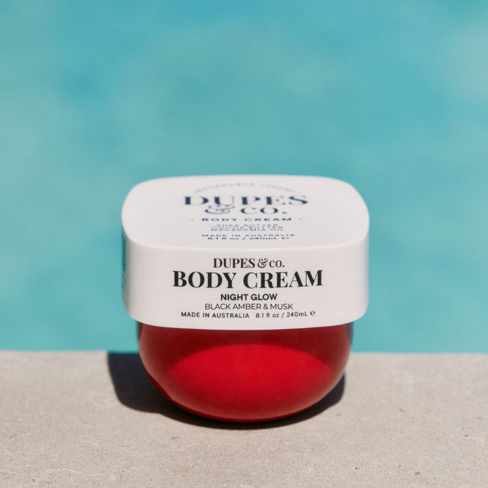 Jar of Dupes & Co. Body Cream with a red interior on a light blue background